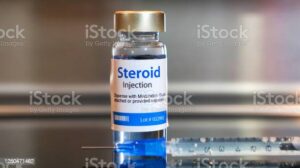 Bottle of Steroid injection with a syringe on black table and stainless steel background