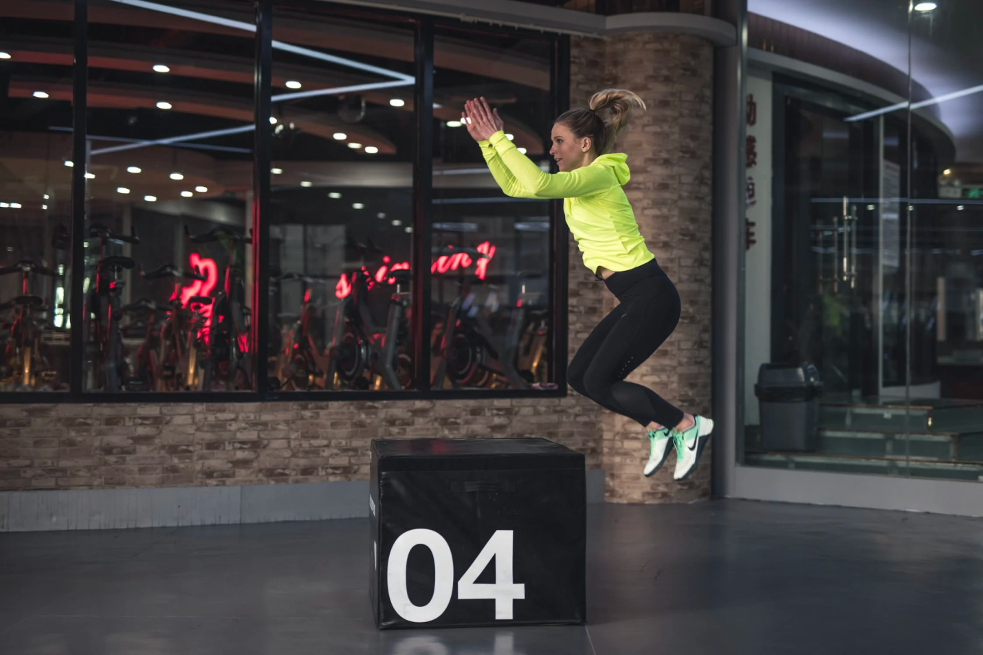a woman performs box jumps on a large cube. 