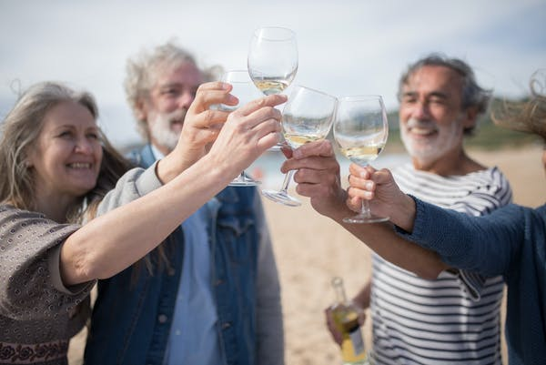 A group of friends toasts with wine glasses at the beach.