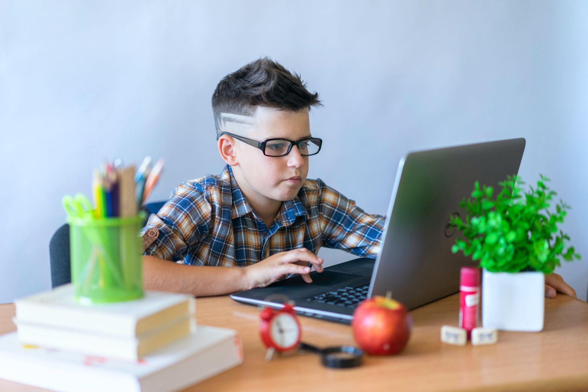 A boy using a laptop while wearing anti-blue light glasses. 