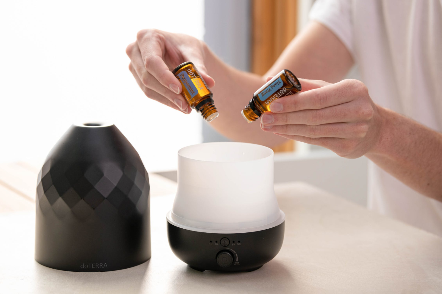  A woman adding two different essential oils to a diffuser