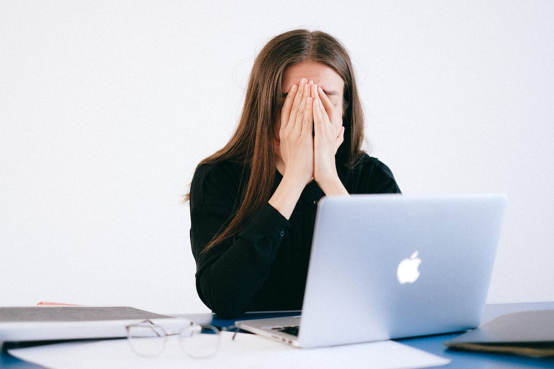 A Visibly Distressed Woman Covering her Face with Both Hands While Facing a Laptop Screen