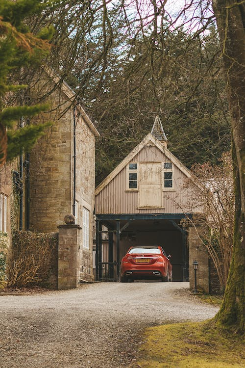 A red colored car stored in an open garage for an old countryside house.