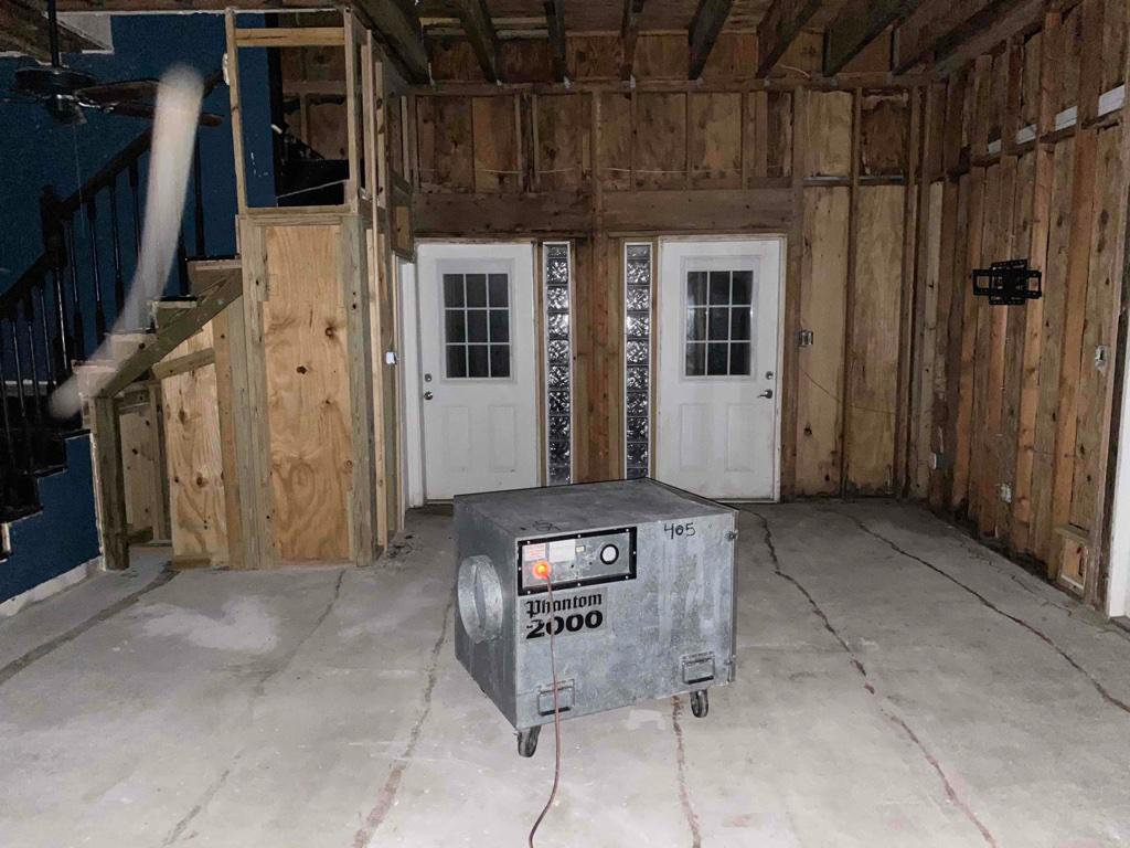 A large silver metal machine with Phantom 2000 on it stands plugged in in the center of a basement stripped of drywall and carpeting with two white doors in front