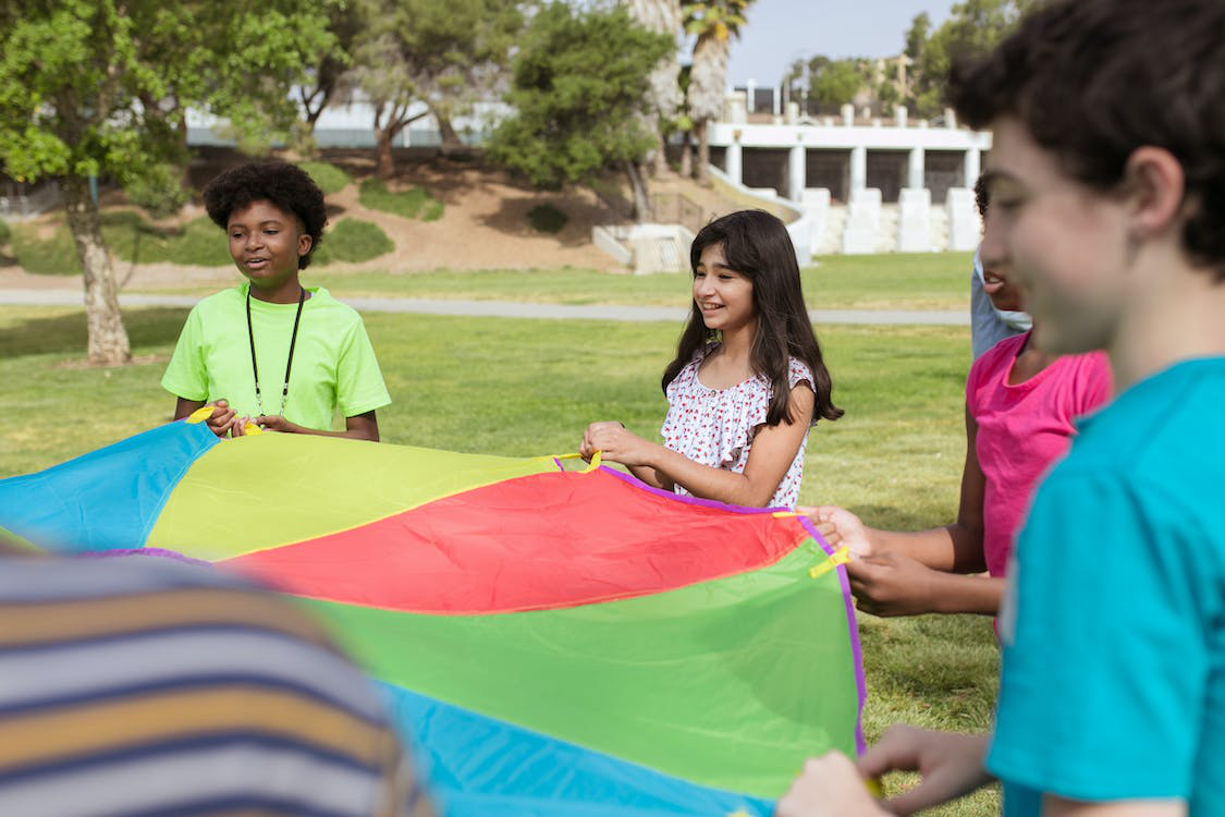 Children from different cultures and backgrounds playing together while holding a parachute tent