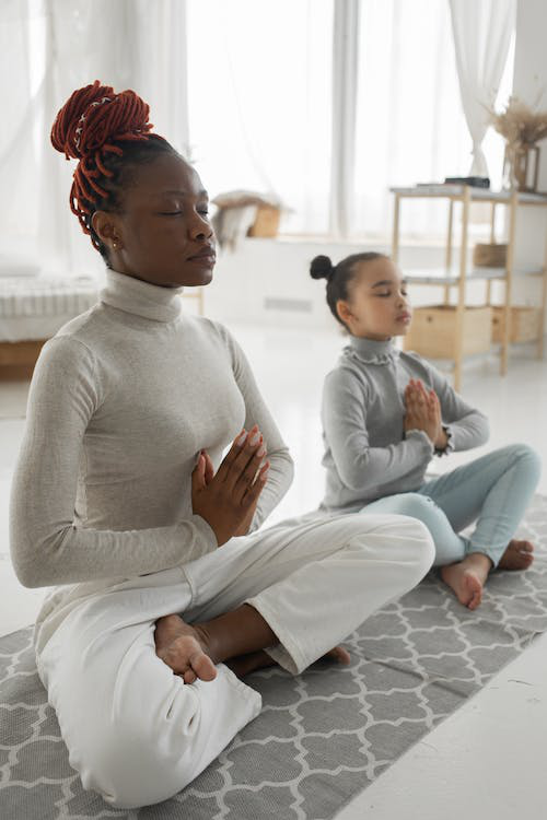 A relaxed woman with her little daughter practicing the Lotus pose at home