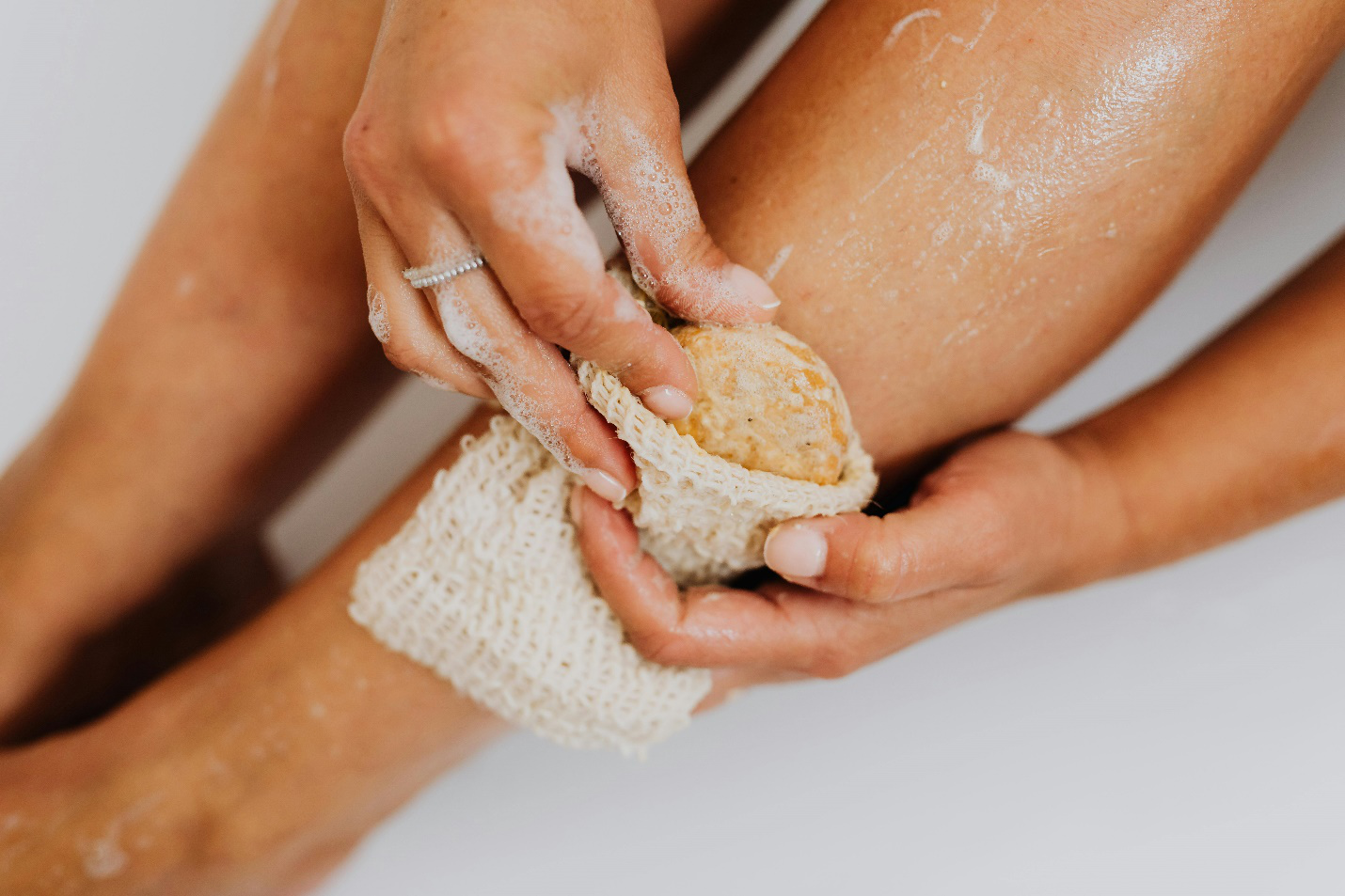  Hand holding soap and scrub, exfoliating leg to prepare for spray tanning service.