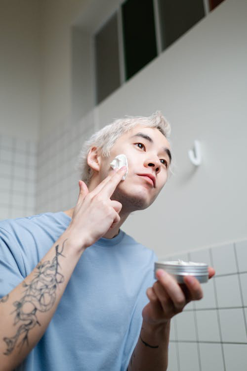 A man applying a thick cream to his face from a jar, representing the modern man’s engagement with high-end skincare products.