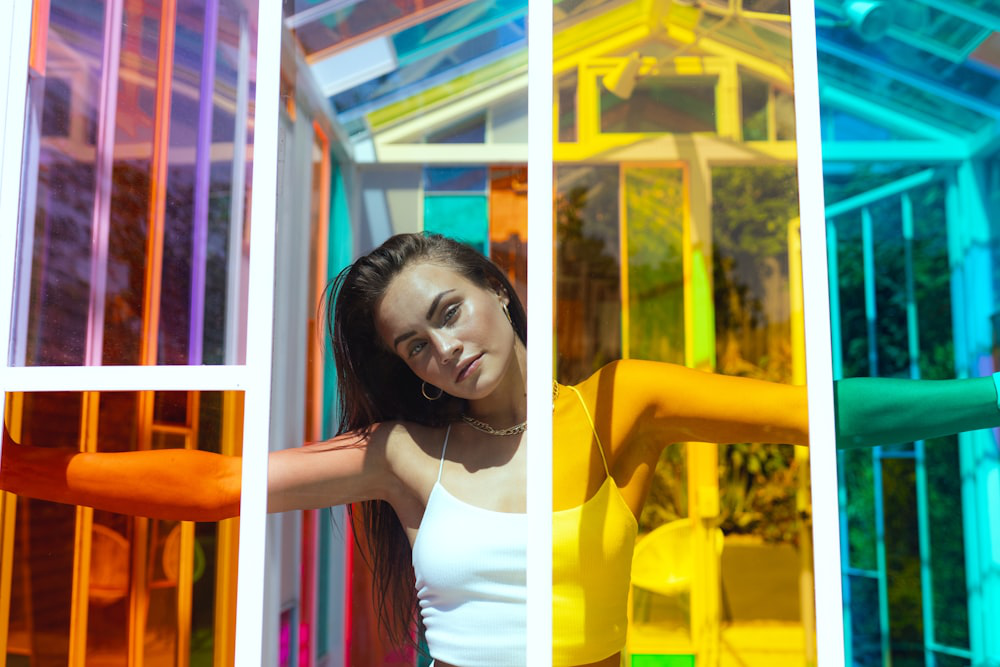 A woman leaning against a white-framed window of a vibrant glasshouse.